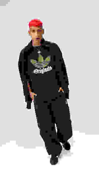 A person wearing a black Originals sweatshirt and red cap stands against a plain white background.