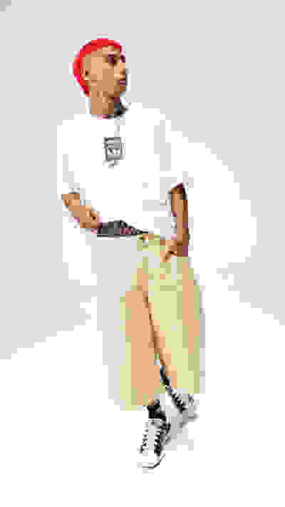 A person wearing a white t-shirt, red hat, and beige pants stands against a plain white background.