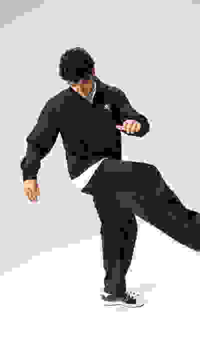 A person wearing a black outfit is performing a dynamic martial arts move, with a plain white background.