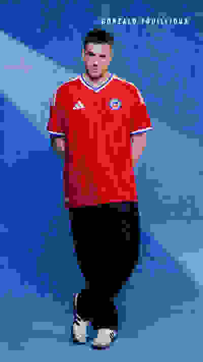 A man wearing a red sports jersey stands in front of a bright blue background.
