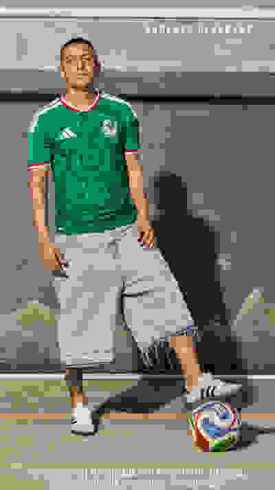 A man wearing a green soccer jersey with a distinctive design stands in front of a painted background, holding a soccer ball.