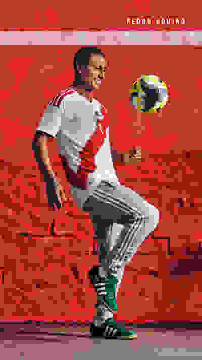 A man in a white jersey and athletic pants stands on a red rocky surface, juggling a soccer ball.