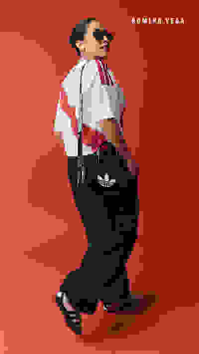 A person wearing a white top with red stripes, black pants, and sunglasses stands against a vibrant red background.