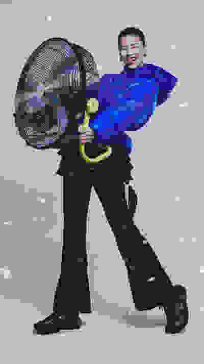 A person in a bright blue costume holding a large fan, standing against a snowy background.