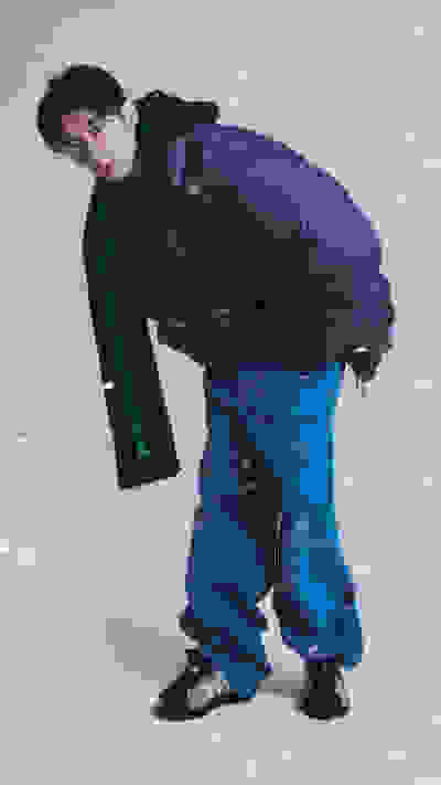 A person wearing a purple jacket and blue pants stands in a snowy outdoor setting, with snowflakes visible in the air around them.