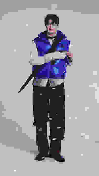 A person wearing a blue and white puffy jacket stands in a snowy outdoor setting, holding an umbrella.