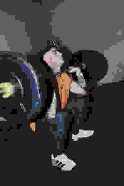 A person in an orange shirt and black pants is lifting a heavy barbell in a dimly lit gym setting.