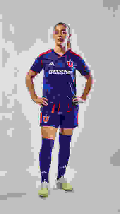 A person wearing a blue and red soccer jersey and shorts, standing with their hands on their hips against a plain gray background.