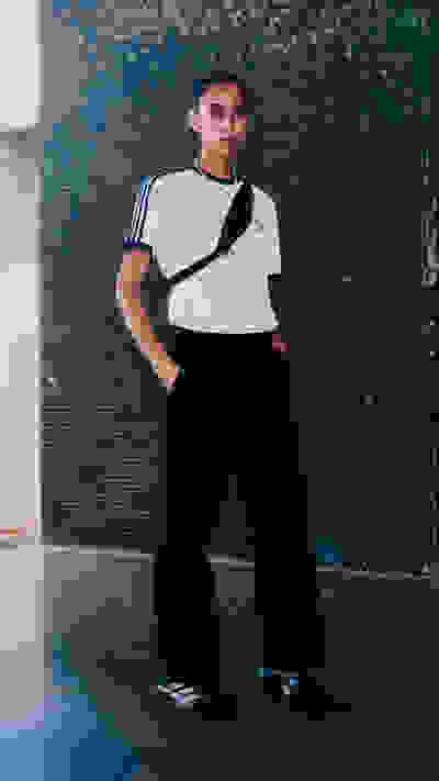 The image shows a person wearing a white t-shirt and black pants, standing in front of a blue tiled wall.