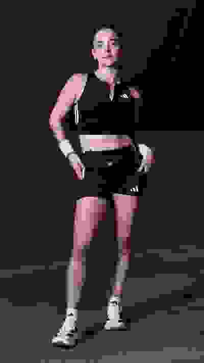 A young woman wearing black athletic clothing and sneakers stands confidently in a dimly lit indoor setting.