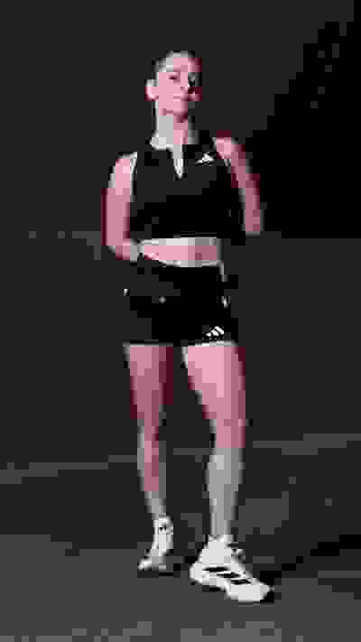 A young woman in athletic clothing stands confidently in a dimly lit indoor setting.