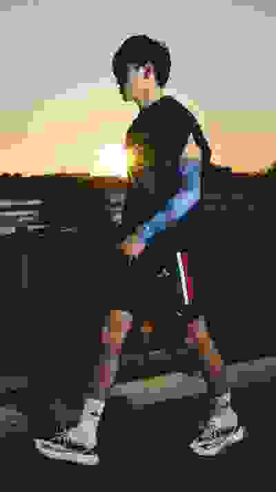 A young man in athletic clothing stands on a wooden deck overlooking a scenic sunset landscape.