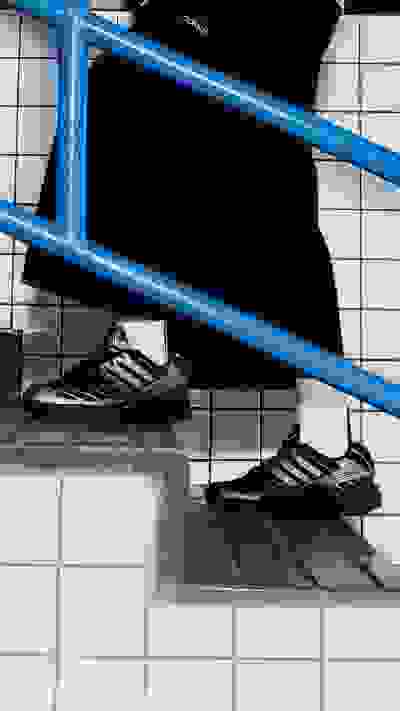A pair of black athletic shoes on a person's feet, standing on a tiled floor with a blue metal ladder in the background.