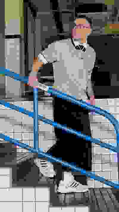 A person wearing a light-colored shirt and glasses is standing on a blue metal staircase in what appears to be a commercial or industrial setting.