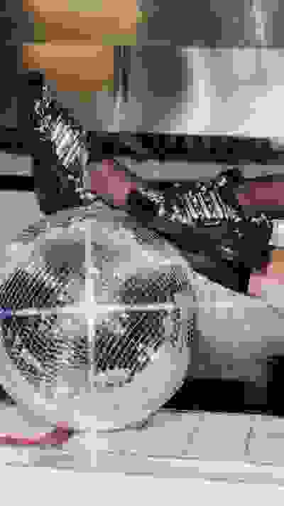 A pair of ornate, patterned shoes rests on a metal grate, with a fan blowing air beneath it.