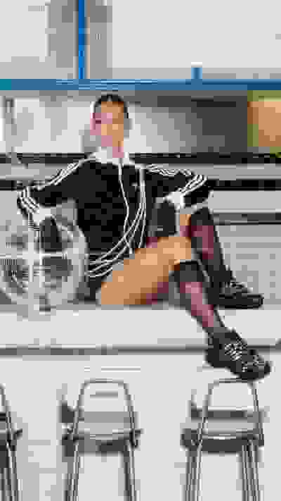 A young woman in a black outfit sits on a shelf in what appears to be a retail or commercial setting, with shelves and displays visible in the background.