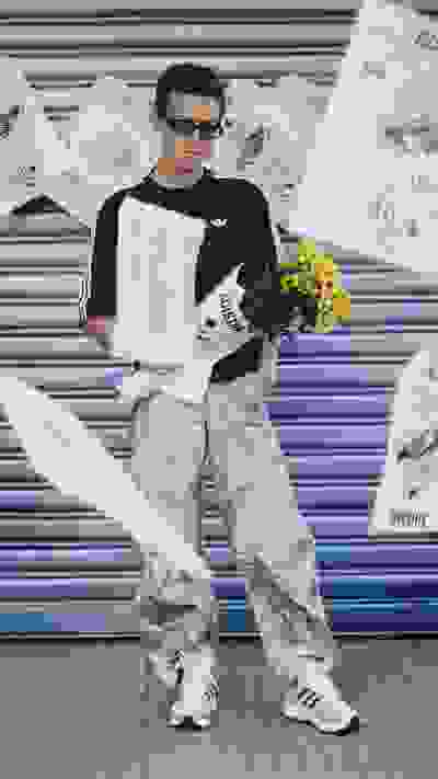 A young man in casual attire stands in front of a metal shutter, holding a bouquet of yellow flowers.