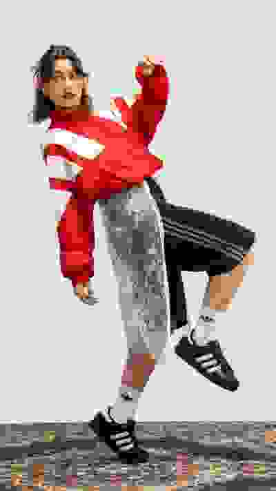 A person wearing a red and white striped sweater and black and white sneakers is jumping and posing in front of a plain white background.