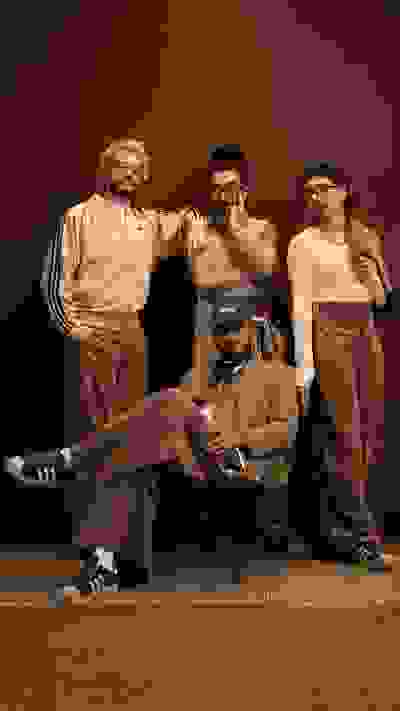 A group of four individuals, dressed in casual attire, are gathered in what appears to be a dimly lit room or studio setting.