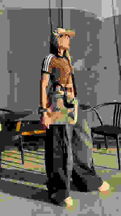 A person wearing a leopard-print top, baggy pants, and a baseball cap stands on a tiled floor in an outdoor setting with chairs and tables in the background.