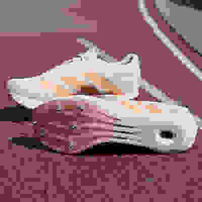 A pair of white and orange athletic shoes with spikes on the soles, resting on a red running track.