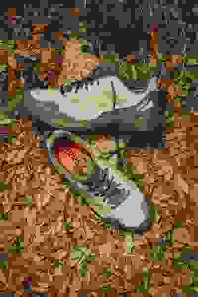 Et par slidte outdoor-vandresko hviler på en skovbund dækket af faldne blade og kviste.