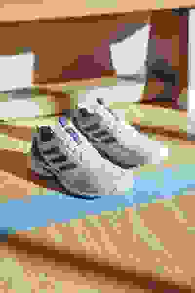 Et par hvide og lilla atletiske sko hviler på et trægulv med en blå yogamåtte i baggrunden.