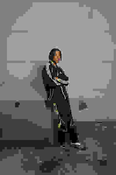 A person wearing a black and neon green athletic outfit stands in front of a plain gray wall.