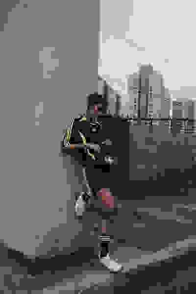 A person in athletic clothing stands against a wall with a cityscape visible in the background.