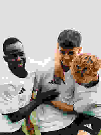 Three young men in sports uniforms embracing and smiling against a blurred outdoor background.