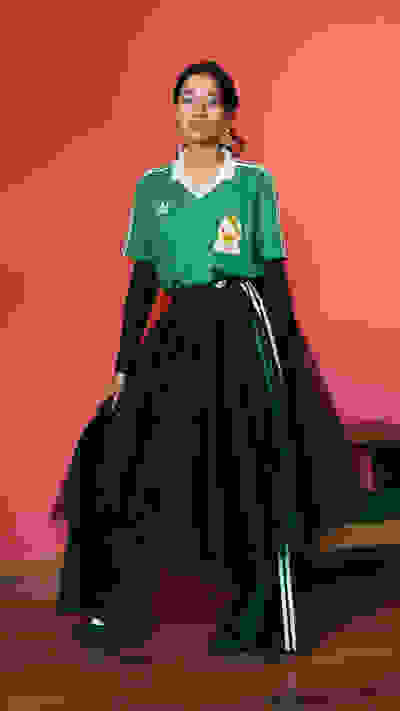 A person wearing a green jersey and a black skirt stands in front of a bright red background.