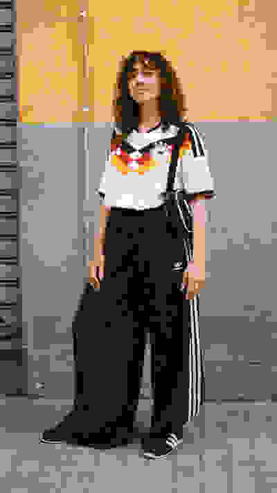 A person wearing a white and black jersey with a German flag design, standing in front of a yellow and gray wall.