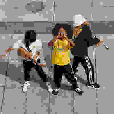 A group of young people, dressed in casual attire, appear to be engaged in some form of musical or artistic performance on a tiled floor.