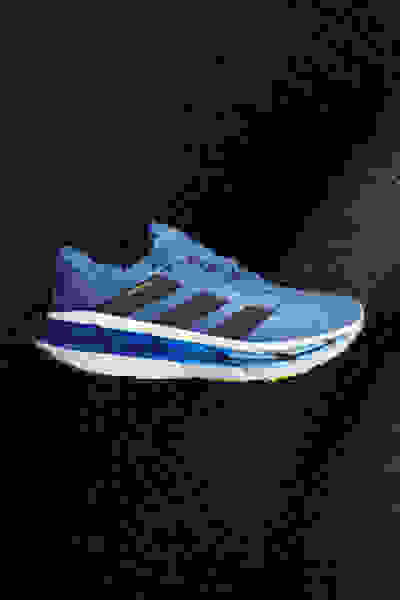 Ein blau-schwarzer Sportschuh mit strukturierter Sohle wird vor einem dunklen Hintergrund präsentiert.