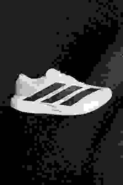 Ein weiß-schwarzer Sportschuh mit dem adidas Logo auf dunklem Hintergrund.