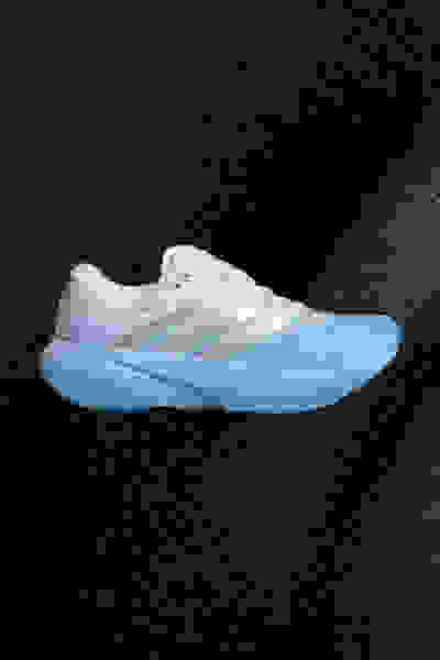 Ein weiß-blauer Sportschuh mit strukturierter Sohle vor einem dunklen Hintergrund.