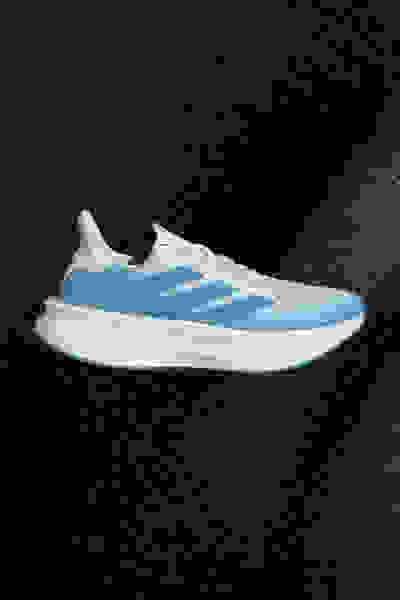 Ein weiß-blauer Sportschuh mit cleanem, modernem Design vor einem dunklen, strukturierten Hintergrund.