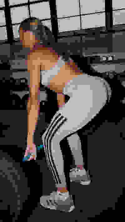 The image shows a woman in athletic wear performing a squat exercise in a gym setting, with large windows in the background.