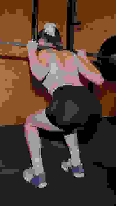 A person in athletic attire is performing a squat exercise on a fitness mat in a gym setting.