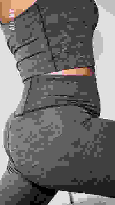 Das Bild zeigt eine Nahaufnahme des unteren Körpers einer Person, die eng anliegende, dunkle Sportbekleidung trägt. Die Kleidung scheint aus einem stretchigen, strukturierten Material zu sein und wird um den Mittelteil und die Beine der Person gewickelt, um die Konturen des Körpers hervorzuheben.