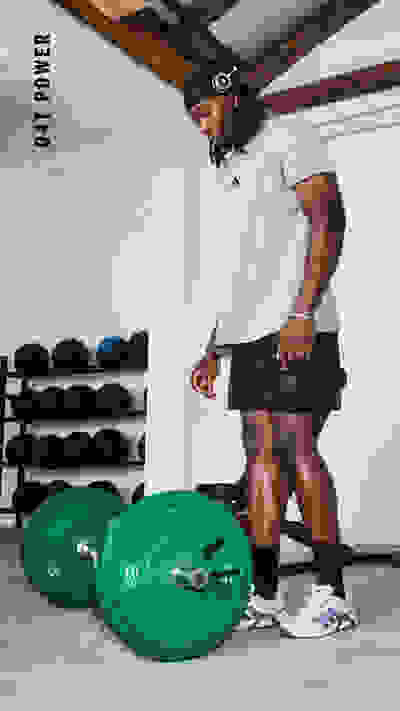 Eine Person in Sportbekleidung hebt eine Reihe grüner Gewichte in einem Fitnessstudio, wobei im Hintergrund Regale mit zusätzlichen Gewichten zu sehen sind.