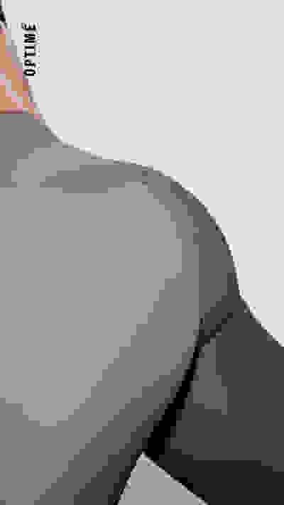 Nahaufnahme des unteren Rumpfs einer Person mit Fokus auf den Rücken und die Beine der Person, wobei graue Sportbekleidung vor einem schlichten Hintergrund getragen wird.  