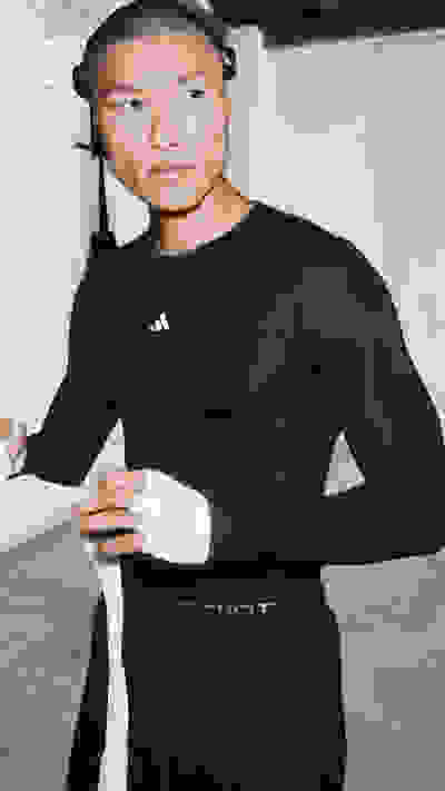 Eine Person, die ein schwarzes Oberteil und eine schwarze Hose trägt, steht in einem Raum mit einer Decke und Wand aus Holz.