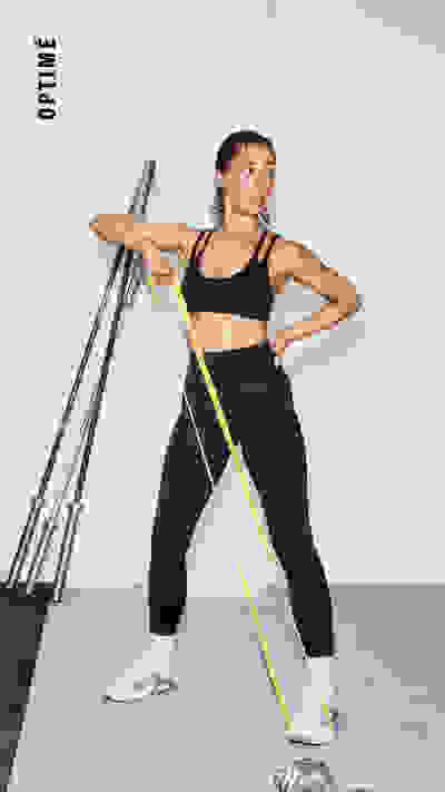 Eine Frau in Sportbekleidung steht im Studio und nutzt Widerstandsbänder für ein Workout.