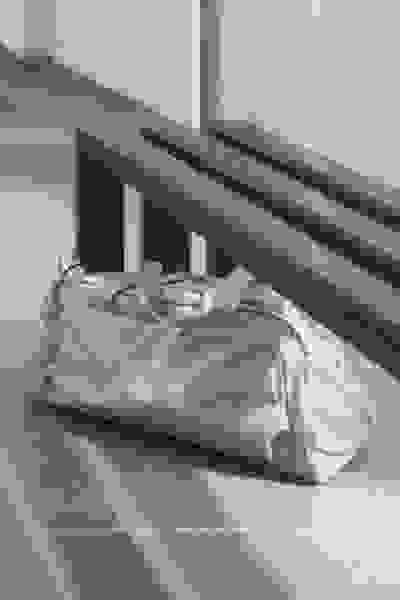 Eine graue Sporttasche sitzt auf einem Fliesenboden vor einer Holzbank vor einer weißen Wand.