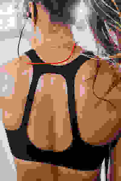 Das Bild zeigt den Rücken einer Person, die einen schwarzen Sport-BH trägt, deren Haare auf dem Rücken gebunden und vor dem hellen Hintergrund sichtbar sind.