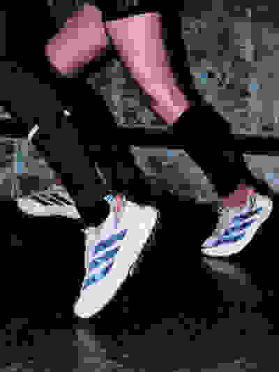 The image shows a person's legs and feet wearing black socks and white and blue sneakers, standing on a concrete surface.