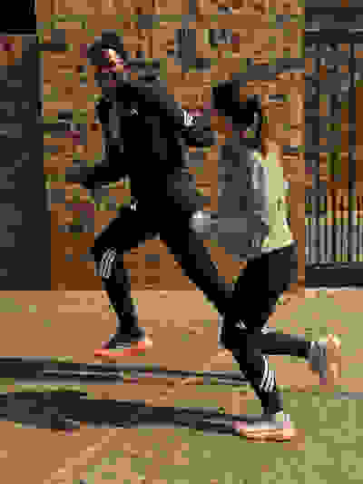 Two people, a man and a woman, are engaged in a physical activity or exercise on a brick-paved surface, with a brick wall in the background.