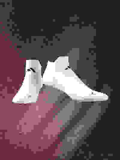 A pair of white athletic shoes with black accents are suspended against a dark, textured background with a reddish hue.