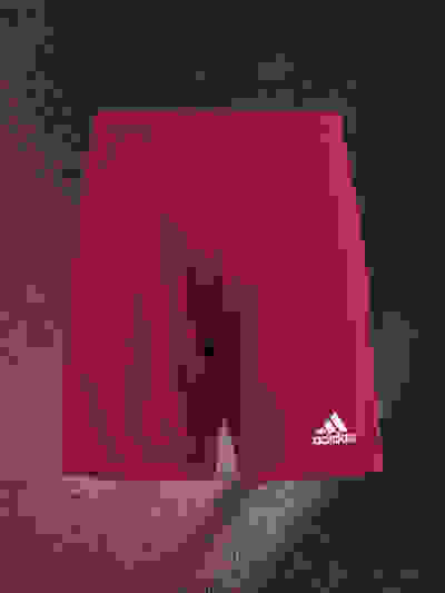 A pair of red Adidas athletic shorts against a dark, textured background.